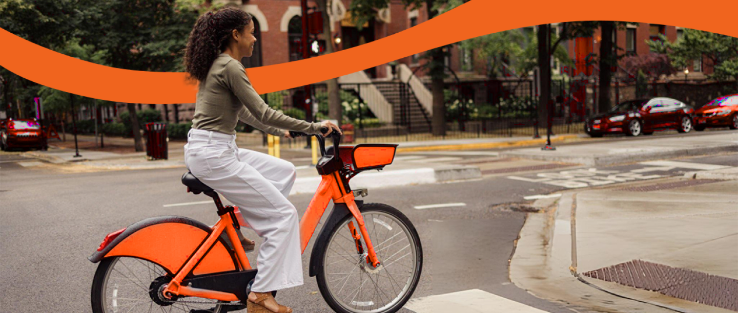 A woman crossing the city on an orange electric bike
