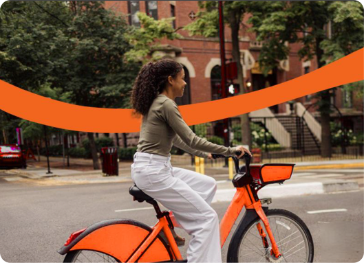 A woman riding an orange ZestRyde bike through the city